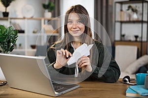 Woman in casual outfit sitting at desk with modern laptop and playing with paper plane