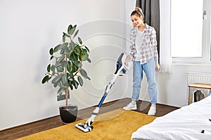 Woman in casual wear vacuum cleaning yellow carpet, tidying white modern living room. Home, housekeeping concept