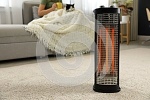 Woman with cat at home  focus on electric halogen heater  closeup