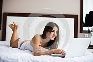 woman catching up on her social media as she relaxes in bed with a laptop computer on a lazy day