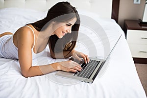 Woman catching up on her social media as she relaxes in bed with a laptop computer on a lazy day