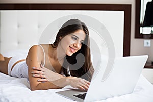 Woman catching up on her social media as she relaxes in bed with a laptop computer on a lazy day