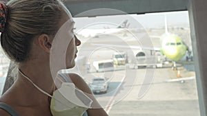 Woman caucasian at airport with wearing protective medical mask on head against the background of the plane. Coronavirus