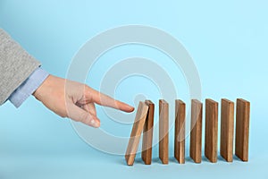 Woman causing chain reaction by pushing domino tile on light blue background, closeup