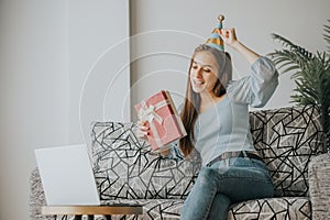 Woman celebrate during video call on laptop at home holding gift box present
