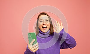 woman celebrating victory holding one fist up wearing casual sweater isolated on pink colored background