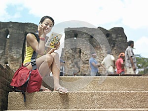 Woman With Cellphone And Guidebook Against Old Ruins