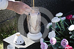 Woman at cemetery is lighting a candle with a match on the grave