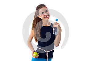 Woman with centimeter around her waist holding apple and water