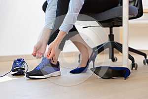 Woman changing high heels, office shoes after working day while sitting on the chair, ready to take a walk or run