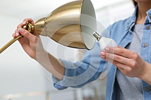 Woman changing light bulb in lamp indoors