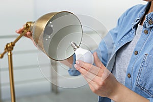 Woman changing light bulb in lamp indoors