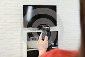 Woman changing TV channel with remote control in living room, focus on hand.