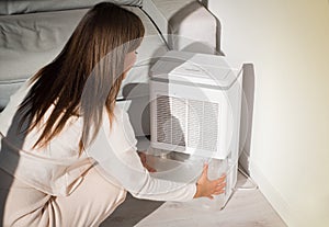 Woman changing water container in air dryer, dehumidifier, humidity indicator. Humid air at home.