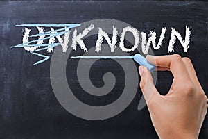 Woman changing the word unknown into known on blackboard photo