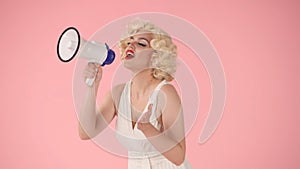 Woman in character of Marilyn Monroe speaking into megaphone. Woman with colorful makeup, wig and white dress in studio