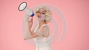 Woman in character of Marilyn Monroe speaking into megaphone. Woman with colorful makeup, wig and white dress in studio
