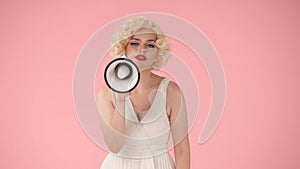 Woman in character of Marilyn Monroe speaking into megaphone. Woman with colorful makeup, wig and white dress in studio