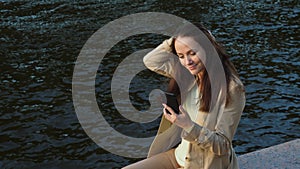 Woman chatting in smartphone, sitting against river park