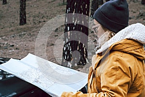 Woman check paper map in the woods forest on the front of the black off road car - concept of people and adventure lifestyle -