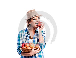 Woman, checked shirt holding basket with fruit. Eating apple.