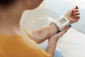 Woman checking blood pressure with sphygmomanometer at home, closeup.