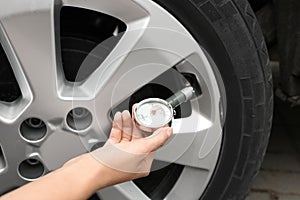 Woman checking car tire pressure with air gauge