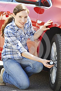 Portrait Of Woman Checking Car Tyre Pressure Using Gauge