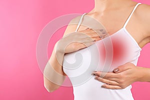 Woman checking her breast on pink background, closeup