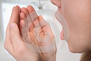 Woman is checking her breath in the palms of hands