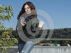 Woman checking her messages and drinking coffee outside