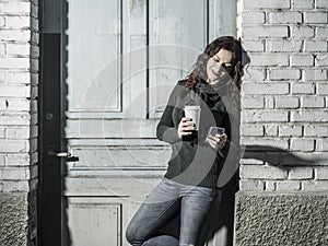 Woman checking her messages and drinking coffee outside