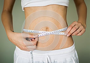 A woman checking her weight loss progress with a measuring tape around her waist. Fitness goals