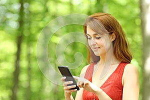 Woman checking phone walking in a green park