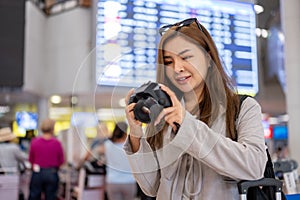 A woman is checking pictures in her camera while walking in the airport, traveling abroad