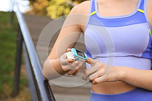 Woman checking pulse with blood pressure monitor on finger after training outdoors, closeup. Space for text