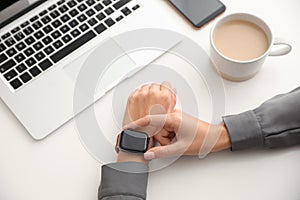 Woman checking stylish smart watch at table, closeup