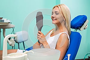 Woman checking teeth in mirror. Female at the dentist office.