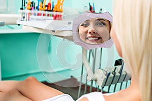 Woman checking teeth in mirror. Female at the dentist office.