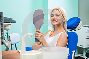 Woman checking teeth in mirror. Female at the dentist office.