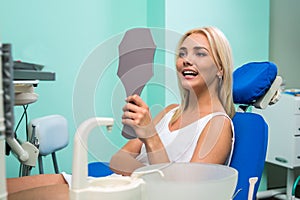 Woman checking teeth in mirror. Female at the dentist office.