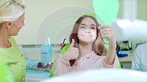 Woman checking their teeth at mirror after dental treatment in dentist office