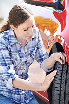 Woman Checking Tread On Car Tyre With Gauge