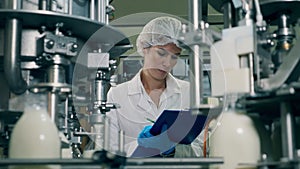 Woman checks bottles with milk on a industrial food and drinks plant conveyor.