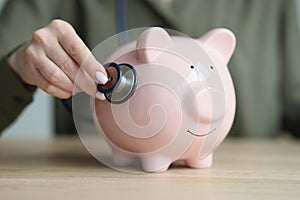 Woman checks condition of piggy bank with stethoscope