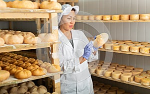 Woman cheesemaker checking aging process of cheese in maturing chamber