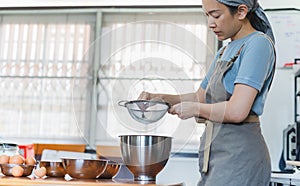 Woman chef with apron sifting flour before making dough.