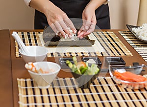 Woman chef filling japanese sushi rolls with rice