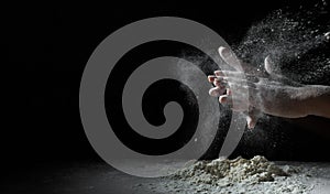 Chef hand clap with splash of white flour and black background with copy space.