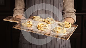 Woman chef holding wooden board with fettuccine nests